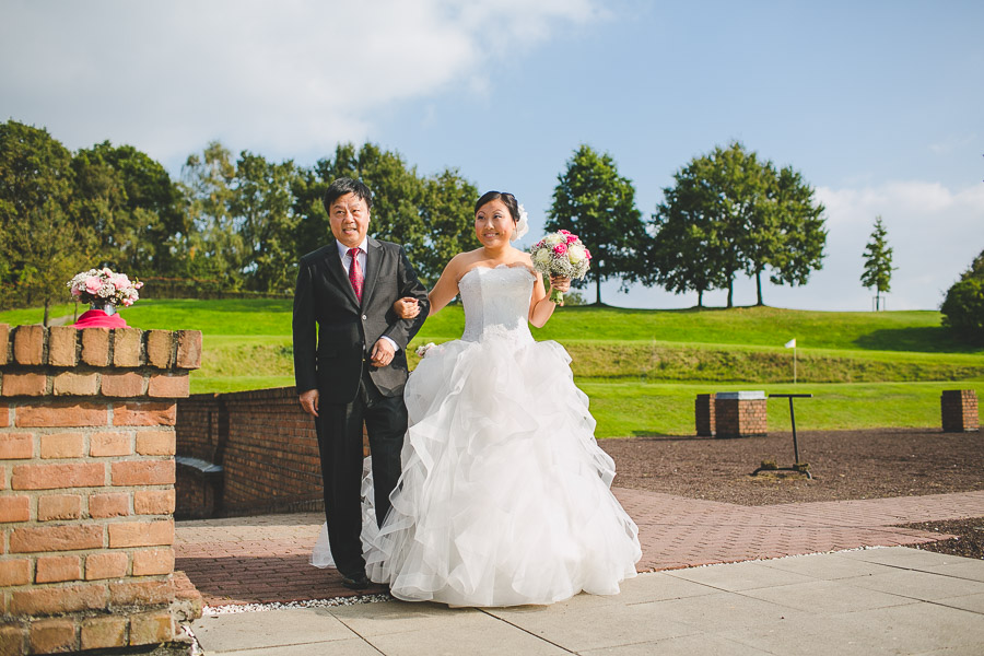 Braut asiatischer Abstammung mit großem Hochzeitskleid à la Prinzessin Sissi wartet mit Vater Chinese kurz vor dem Einzug freie Zeremonie bei Sonnenschein