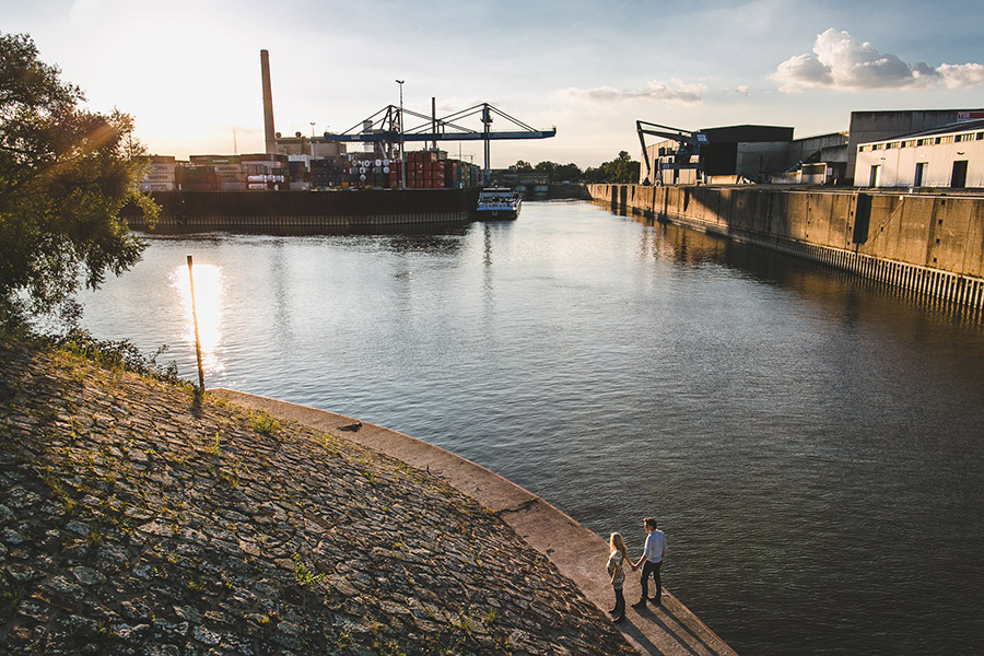 Pärchen mit schwangeren Frau hält Händchen. Im Hintergrund der Industrie Hafen in Düsseldorf beim Sonnenuntergang. Perspektive von oben.