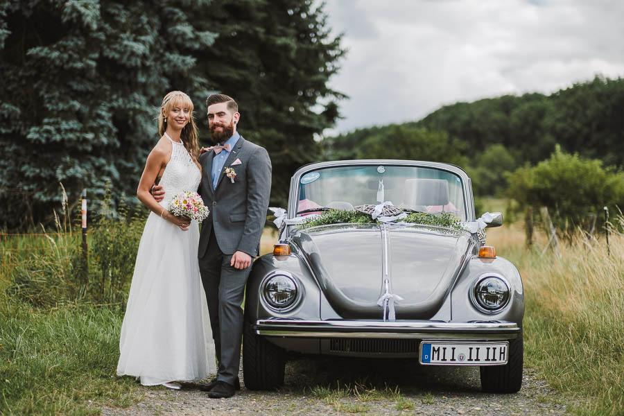 Brautpaar posiert am VW Käfer als Hochzeitsauto