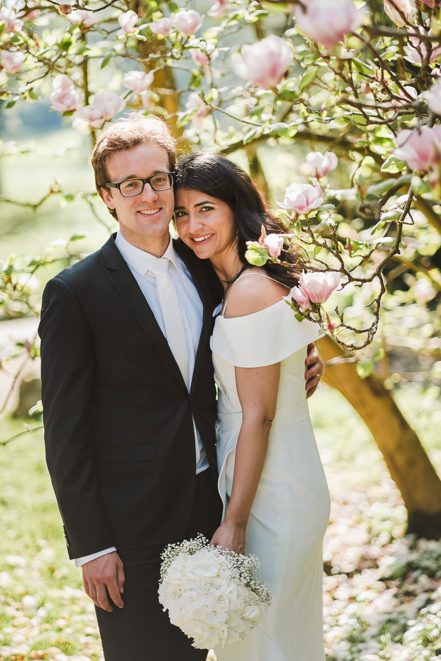 Brautpaar lächelt beim Fotoshooting vor Pfingstbaum