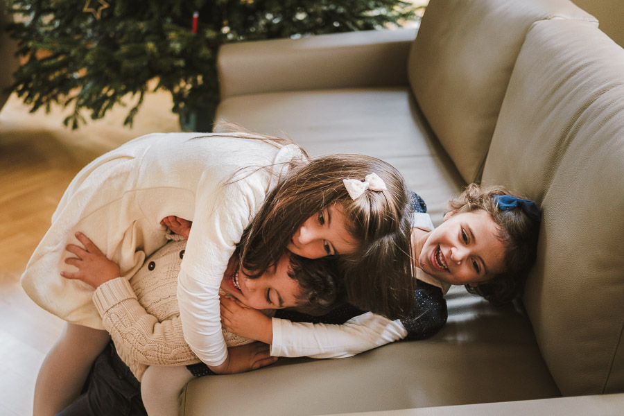Drei Kinder kuscheln spielerisch auf dem Sofa – natürliche und fröhliche Weihnachtsfotos